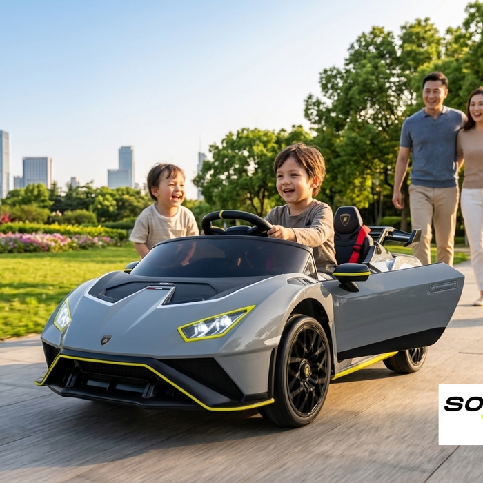 A happy child driving an officially licensed gray Lamborghini Huracán STJ kids' ride-on car on a park pathway, with illuminated LED headlights, an open side door, and a smiling family in the background.