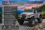 Classic grey 1974 Toyota Land Cruiser FJ40 kids 24V ride-on truck with off-road rubber tires, round headlights, and roof spotlight bar parked on a rocky trail with mountains in the background