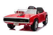 A red 1970-style muscle car ride-on toy with black seats, a clear windshield, chrome-style wheels, and a decorative hood prop, photographed on a white studio background.