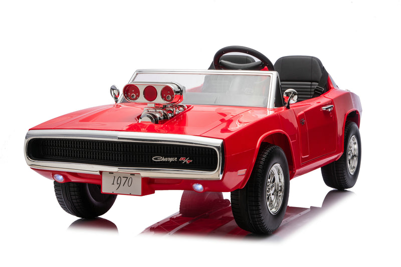 A red 1970-style muscle car ride-on toy with black seats, a clear windshield, chrome-style wheels, and a decorative hood prop, photographed on a white studio background.