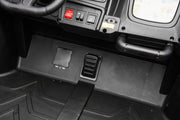 Close-up of a black plastic vehicle or machinery footwell area with a black floor mat, control switches, a red button, and a handle.