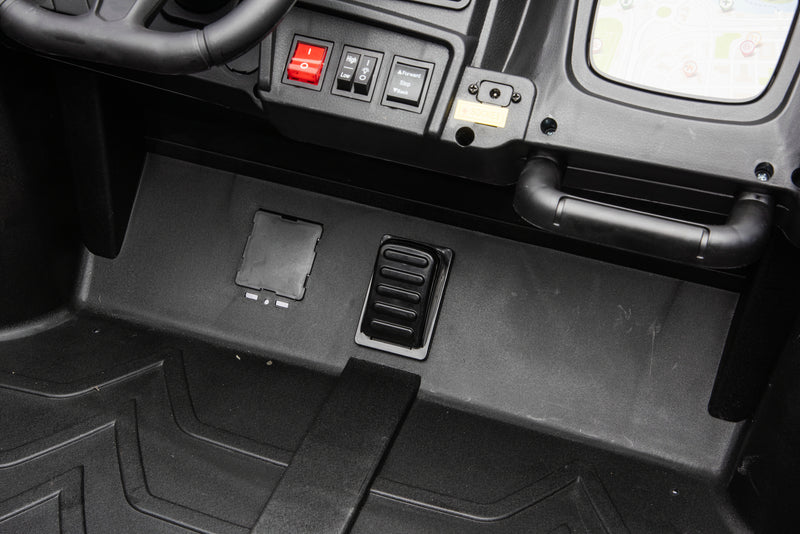 Close-up of a black plastic vehicle or machinery footwell area with a black floor mat, control switches, a red button, and a handle.