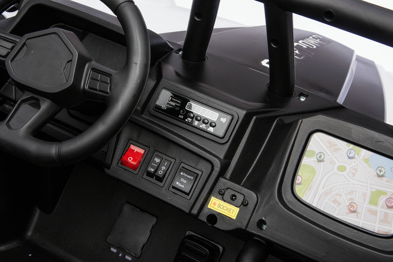 Close-up of a black electric ride-on toy vehicle dashboard, featuring a steering wheel, control buttons, a red start/stop switch, and a screen displaying a map.
