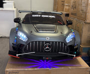 Front profile shot of the Mercedes-Benz AMG GT 24V Drift Edition electric ride-on car in matte grey, equipped with a wide-body kit and an LED underglow