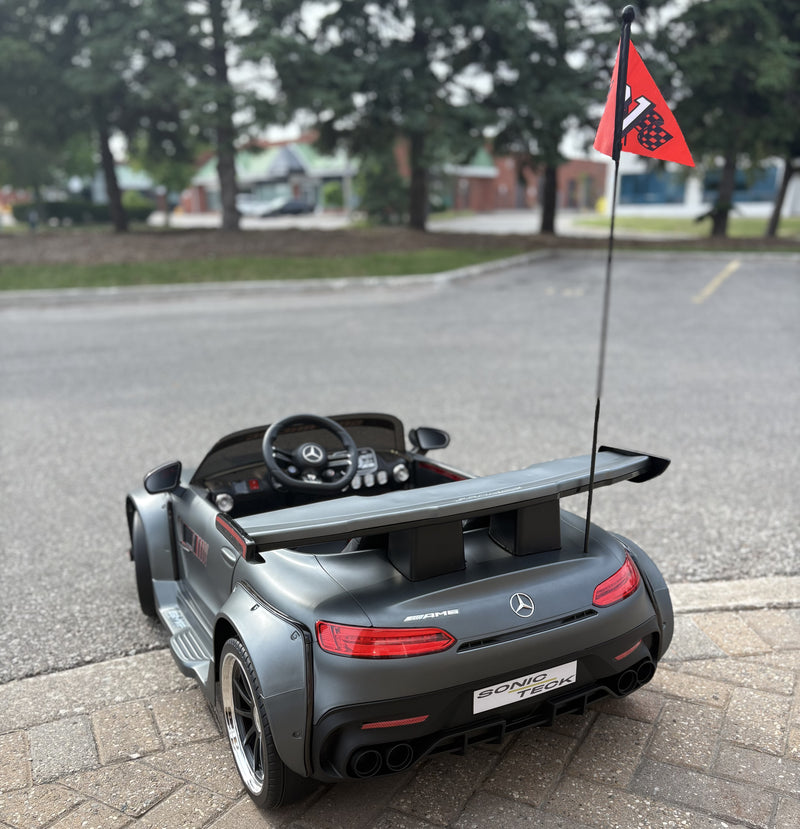 Outdoor shot focusing on the rear profile of the matte grey Mercedes-Benz AMG GT ride-on toy, featuring detailed tail lights, rear diffuser, and safety flagpole