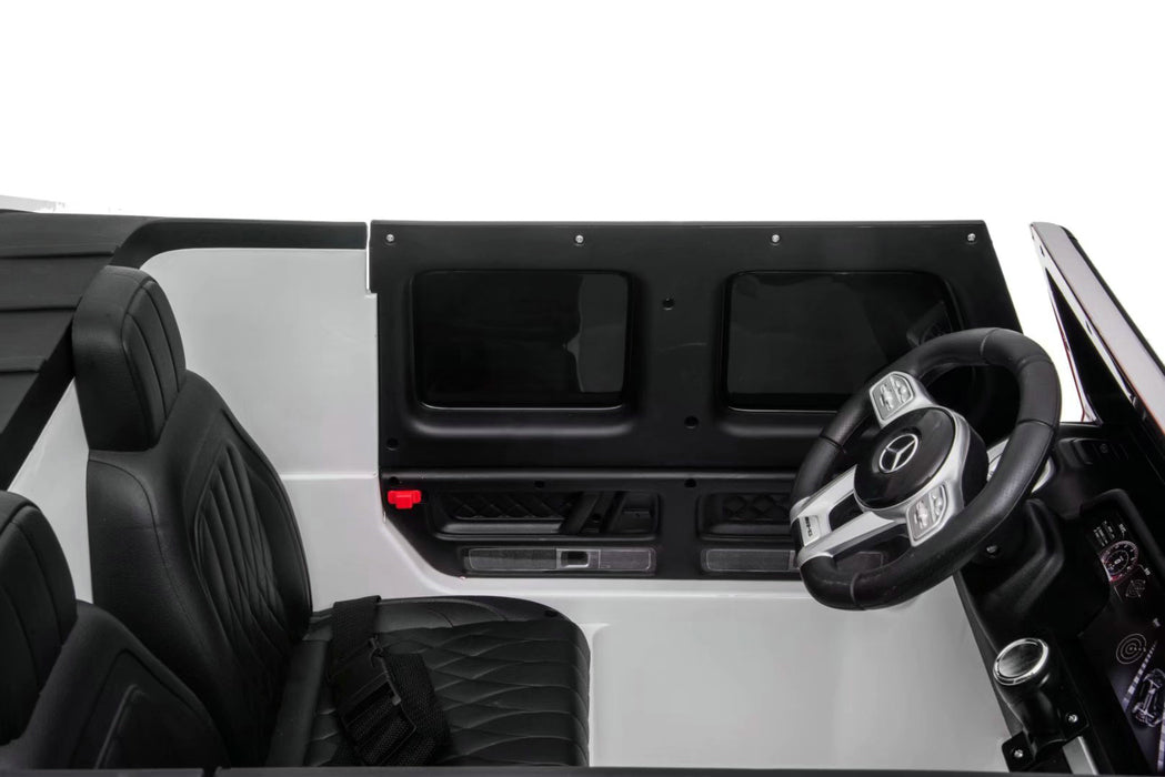 Interior of Mercedes G63 ride-on car showing two leather seats and seatbelts for kids.