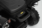 Close-up of a black electric ride-on toy vehicle showing the storage compartment, textured step handle, suspension, and rugged tire against a light gray background.